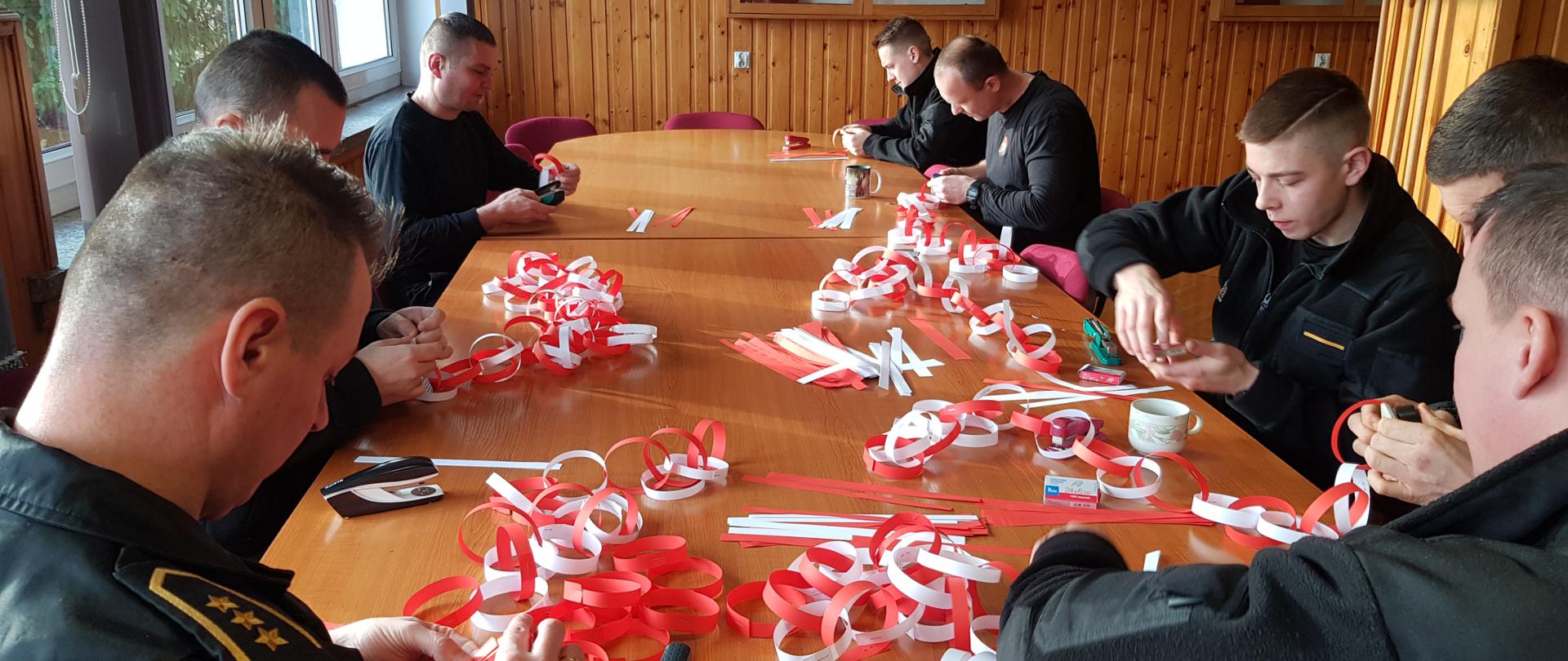 funkcjonariusze PSP siedzą przy stole i robią łąńcuch choinkowy
