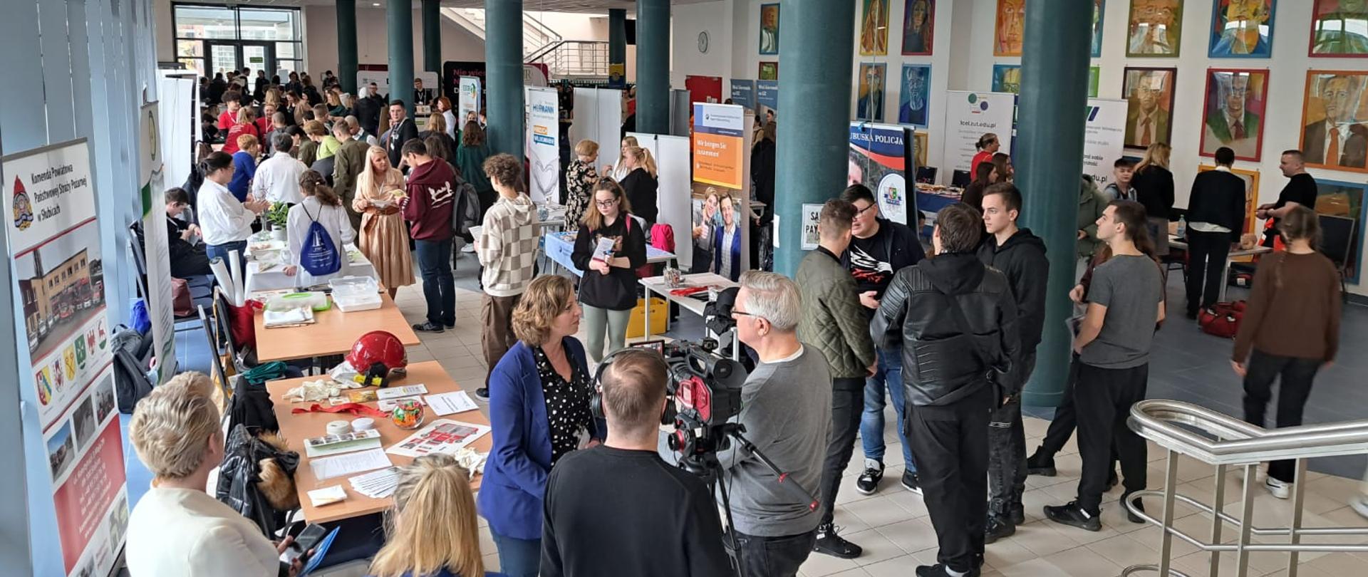 Wnętrze Collegium Polonicum w Słubicach. Widok z góry na stoiska promocyjne szkół, zakładów pracy i instytucji. Duża ilość młodzieży i osób dorosłych przy stoiskach.
