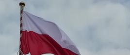 Biało czerwona flaga na szczycie masztu. W tle niebo.