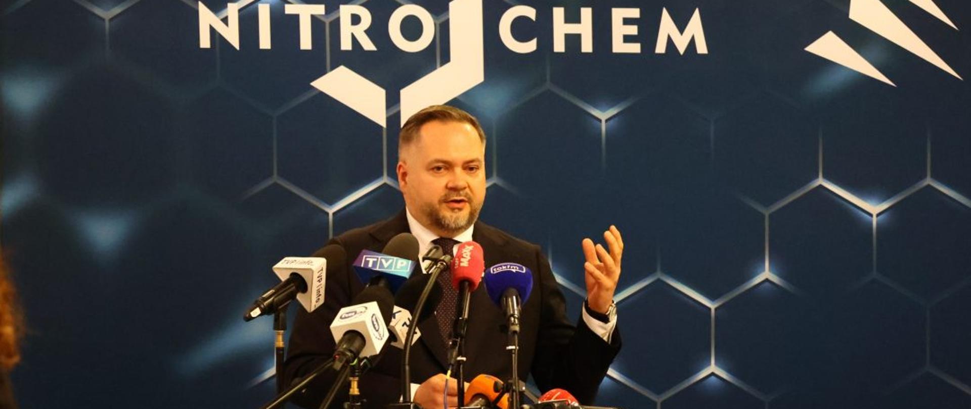 Wiceminister Konrad Gołota stoi za mównicą. W tle ścianka z logotypem Nitrochem.