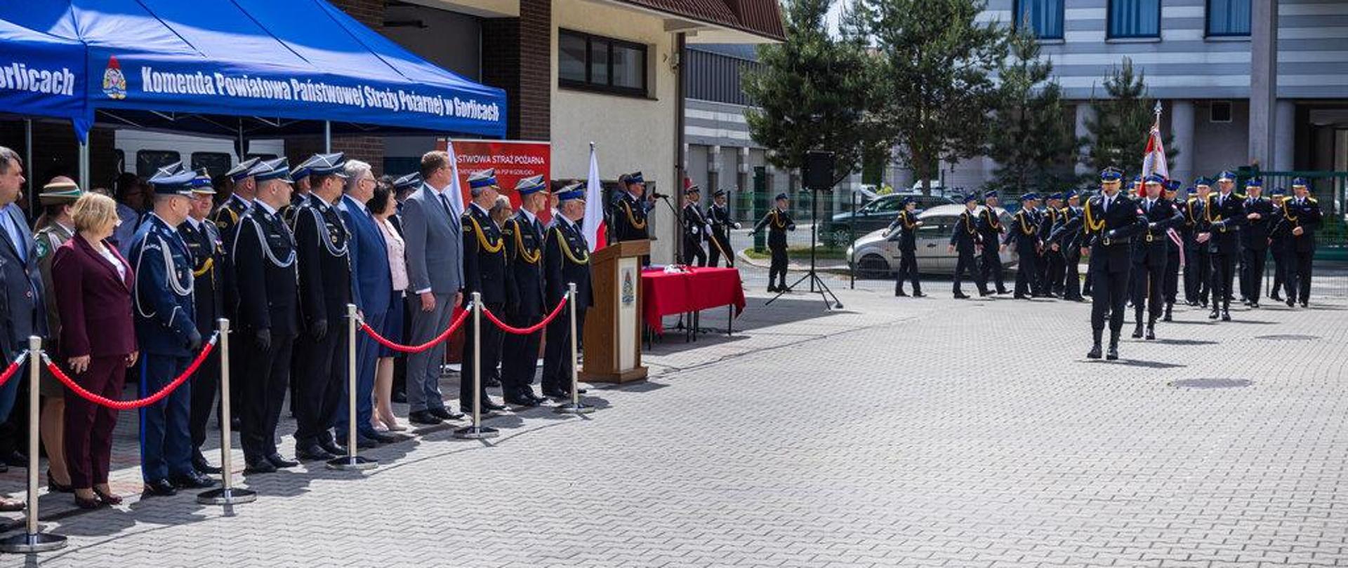 Na zdjęciu widoczny pododdział składający się ze strażaków z Komendy Powiatowej Państwowej Straży Pożarnej podczas defilady z okazji Dnia Strażaka 2024 r. Zaproszeni na uroczystość goście w tym mundurowi obserwują defiladę.