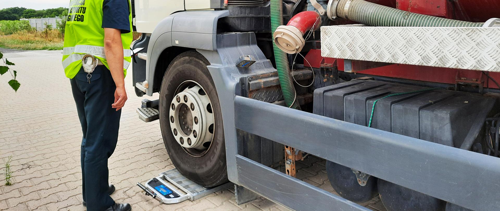 Sprawdzenie wagi pojazdu asenizacyjnego, zatrzymanego przez patrol dolnośląskiej ITD. W centrum pojazd, na inspekcyjnych przenośnych wagach sprawdzana jest pierwsza oś pojazdu. Na wysokości kabiny kierowcy stoi inspektor ITD i odczytuje wynik.