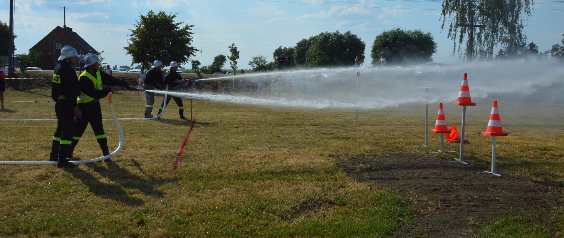Zawody gminne w Śląskowie. Na placu ćwiczeń rozgrywane jest ćwiczenie bojowe. Roty gaśnicze wykonują swoje zadania, tj. przy pomocy wody obracają tarczę oraz strącają pachołki ustawione na postumentach. 