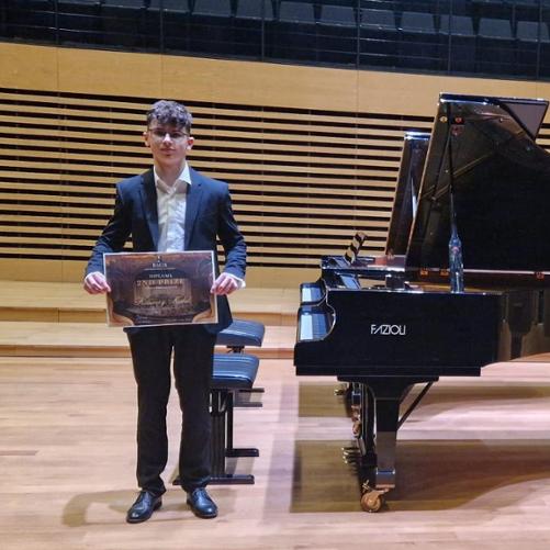 Ksawery Kubik stojący obok fortepianu z dyplomem z konkursu
