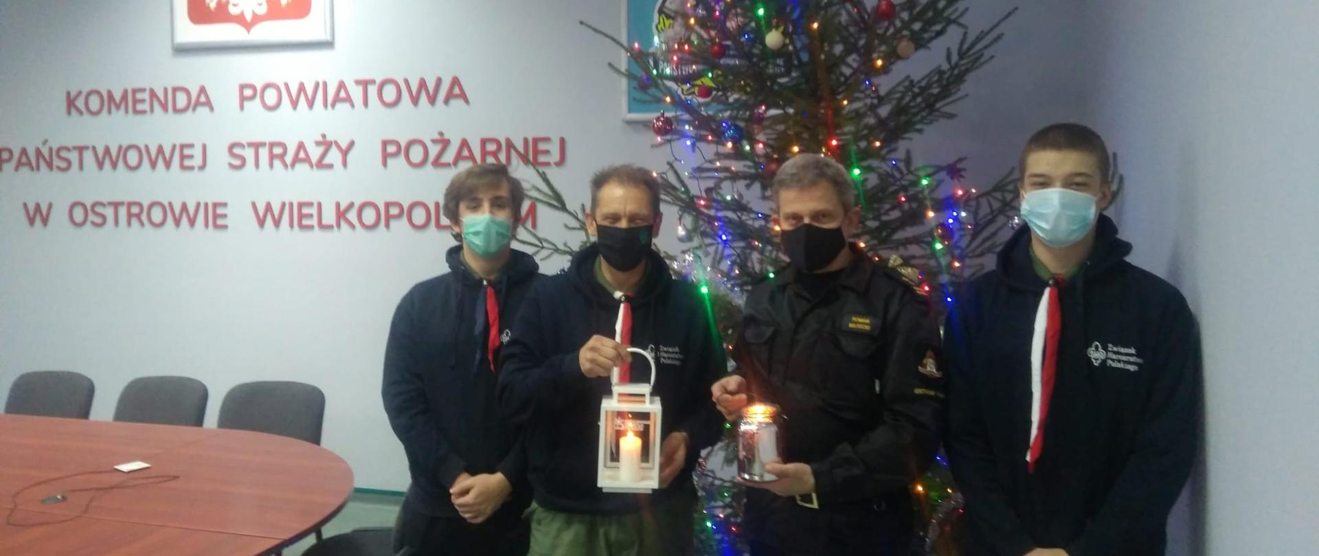 Harcerze z Hufca ZHP oraz komendant trzymający w rękach światełko betlejemskie w tle dekoracja świąteczna
