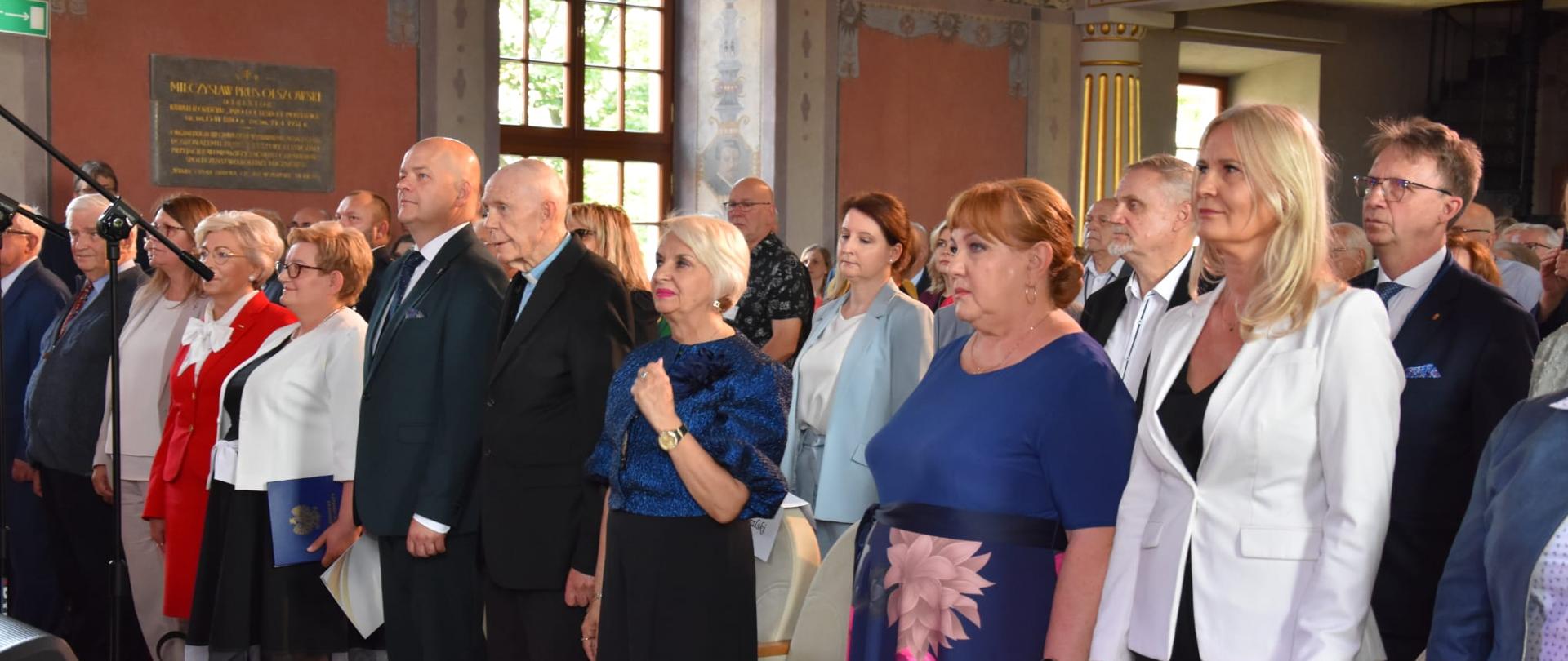 zdjęcie w auli, grupa ludzi stoi na baczność