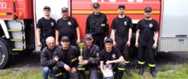 Zdjęcie przedstawia druhów OSP Marcinkowice z pucharem i dyplomem, na tle samochodu pożarniczych