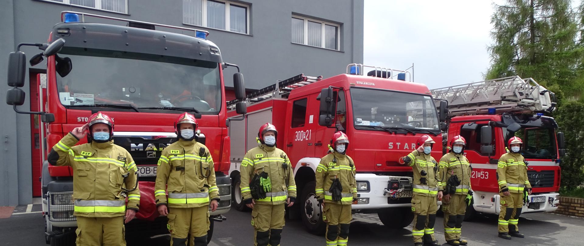 strażacy oddają honor w tle pojazdy ratowniczo - gaśnicze 