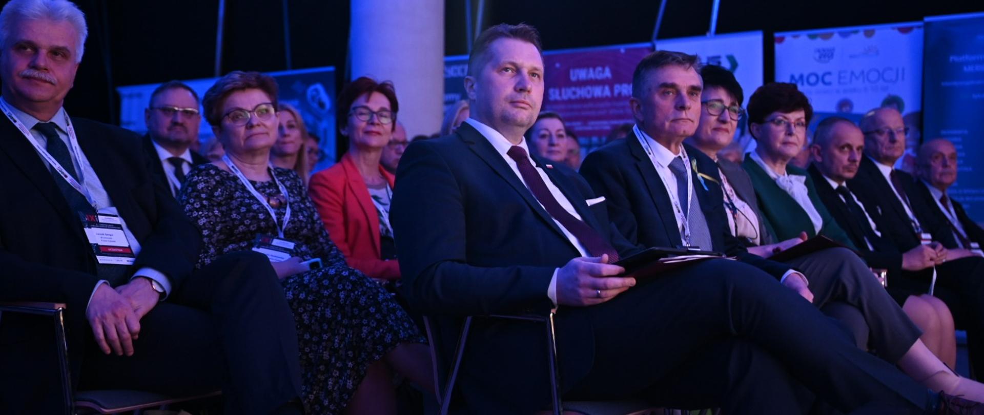 Minister Przemysław Czarnek siedzi na widowni wśród innych uczestników konferencji.