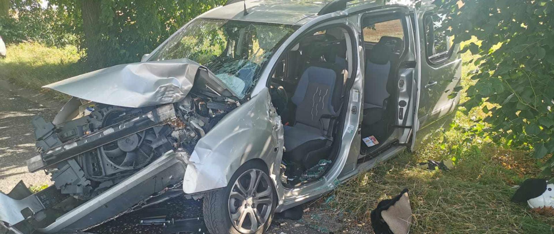 Zdjęcie przedstawia zniszczony samochód osobowy po uderzeniu w drzewo