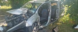 Zdjęcie przedstawia zniszczony samochód osobowy po uderzeniu w drzewo