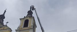 Rozstawiona drabina mechaniczna z koszem na wysokości wierzy kościelnej