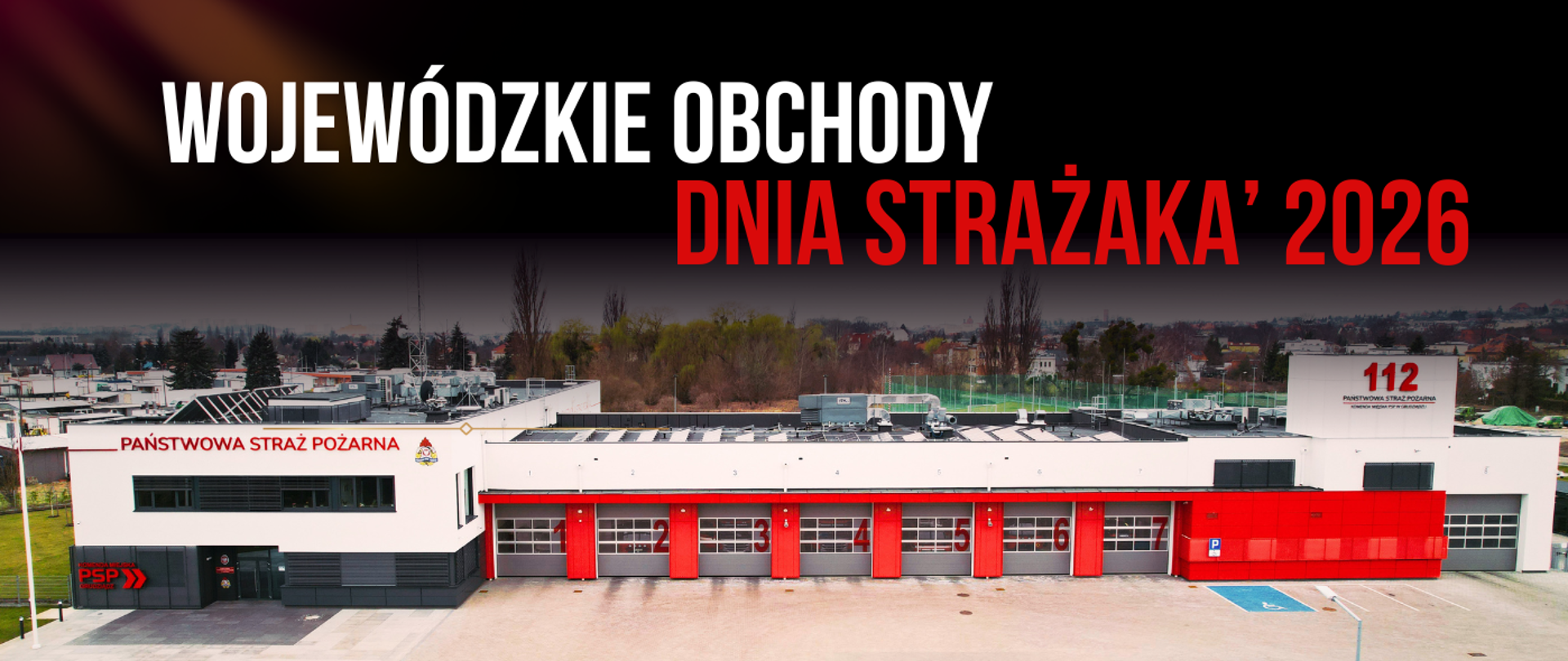 Budynek strażnicy z placem manewrowym. Widok na 7 bram garażowych, a z lewej strony piętrowa część administracyjna. W dali drzewa, zabudowania. Na górze napis Wojewódzkie Obchody Dnia Strażaka