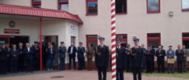 Zaproszeni goście podczas uroczystej zbiórki z okazji Dnia Strażaka stoją przed budynkiem Komendy Powiatowej PSP w Człuchowie. Przy maszcie stoi poczet flagowy.