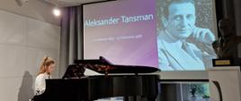 Martyna Sidorów grająca na fortepianie. W tle na wysuniętym ekranie wyświetlony slajd z napisem Aleksander Tansman i podanymi datami urodzin i śmierci oraz zdjęcie biało-czarne patrona szkoły. Z prawej strony widać popiersie Aleksandra Tansmana na białym postumencie a przed nim logo szkoły. 