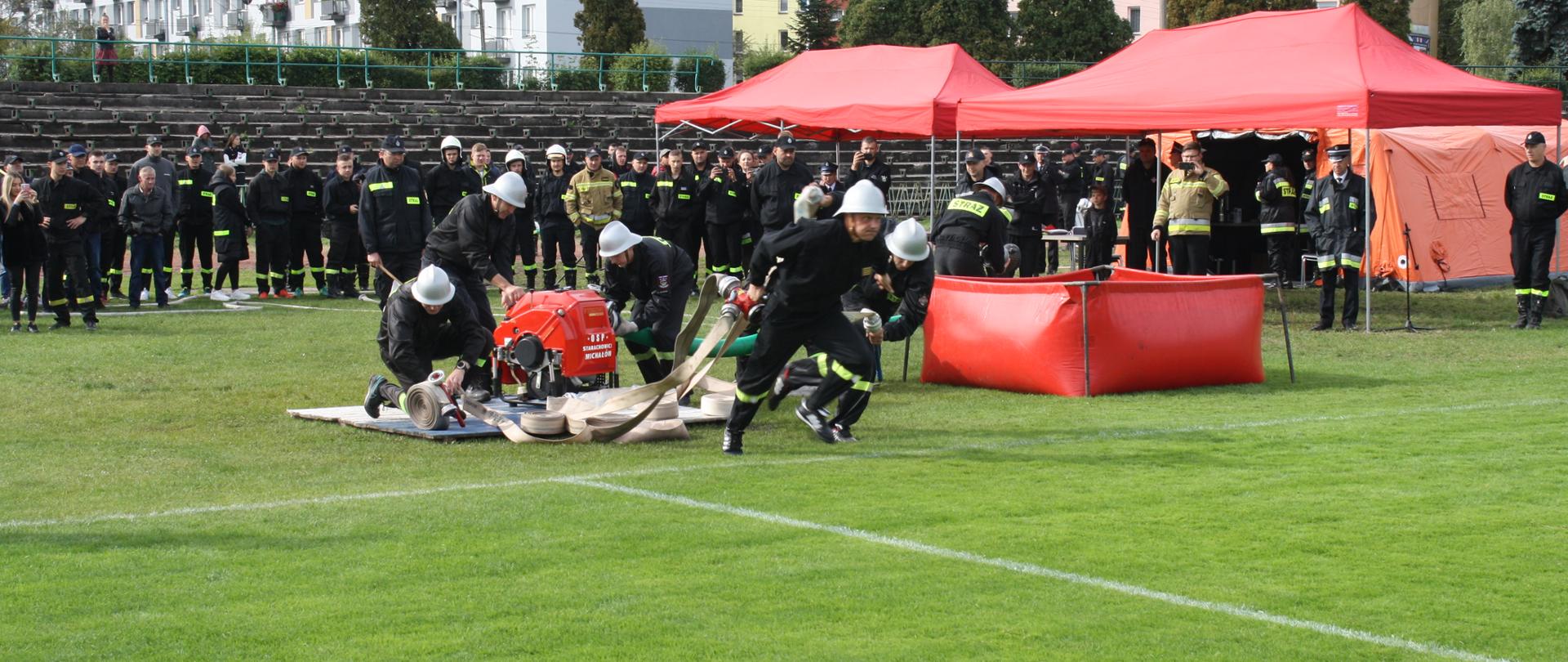 Strażacy OSP dobiegający do podestu z ustawionym sprzętem pożarniczym w ćwiczeniu bojowym