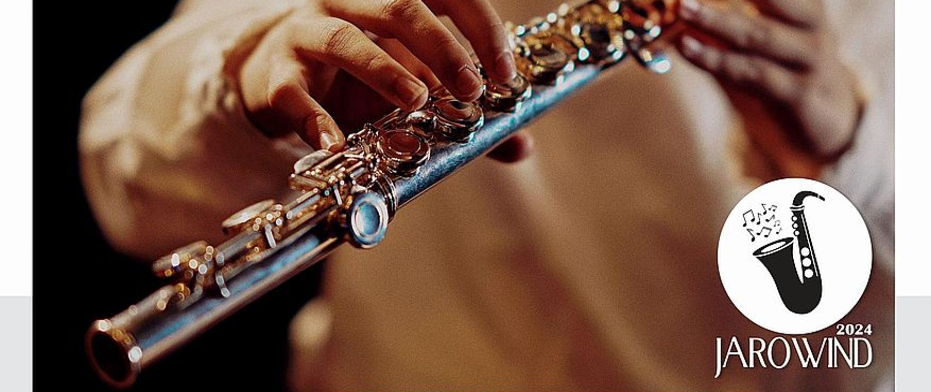 Na zdjęciu widać ręce osoby trzymającej flet poprzeczny. W prawym dolnym rogu umieszczono logo konkursu Jarowind. Poniżej znajdują się informacje o szczegółach konkursu. 