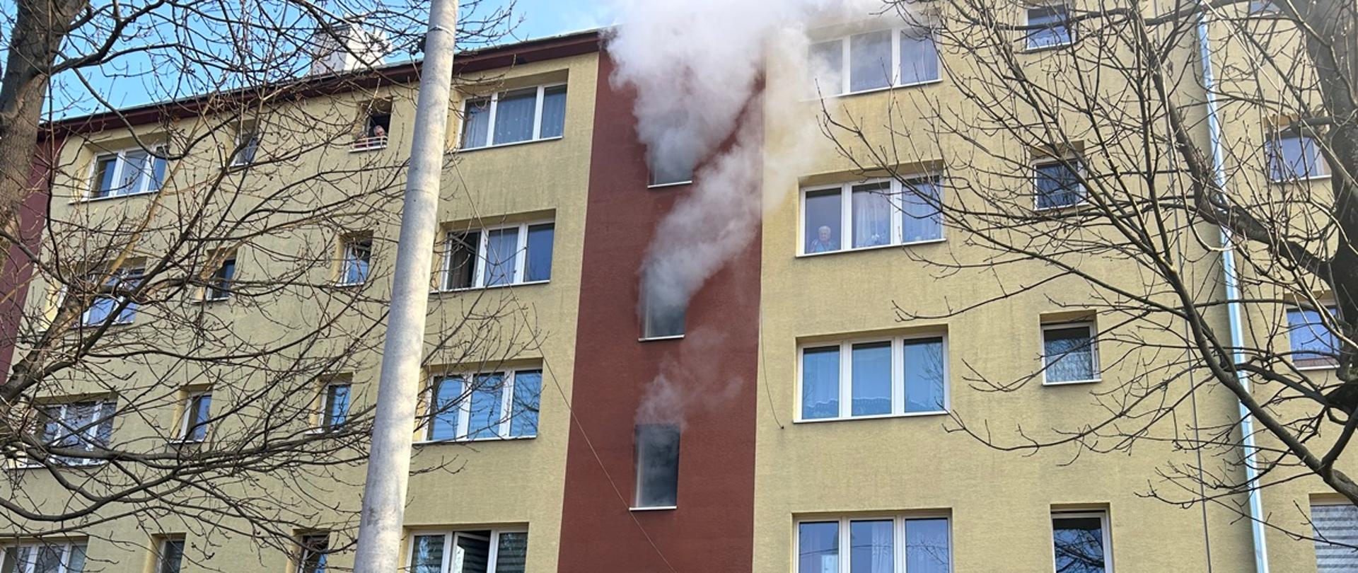 Na zdjęciu blok mieszkalny. Z okien wydobywa się dym.