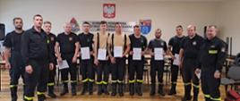 Zdjęcie przedstawia strażaków w umundurowaniu koszarowym, na sali szkoleniowej. Strażacy trzymają w ręku zaświadczenia o ukończonym egzaminie.
