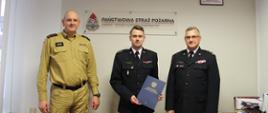Na zdjęciu stoją od lewej: zastępca kujawsko kujawsko-pomorskiego komendanta wojewódzkiego PSP st. bryg. Sławomir Herbowski p.o. zastępcy komendanta powiatowego PSP w Wąbrzeźnie kpt. Robert Stasiak oraz kujawsko-pomorski komendant wojewódzki PSP st. bryg. Jacek Kaczmarek. Strażacy stoją na tle ściany nas nimi napis Państwowa Straż Pożarna. Nowo powołany zastępca trzyma w ręku akt powołania.