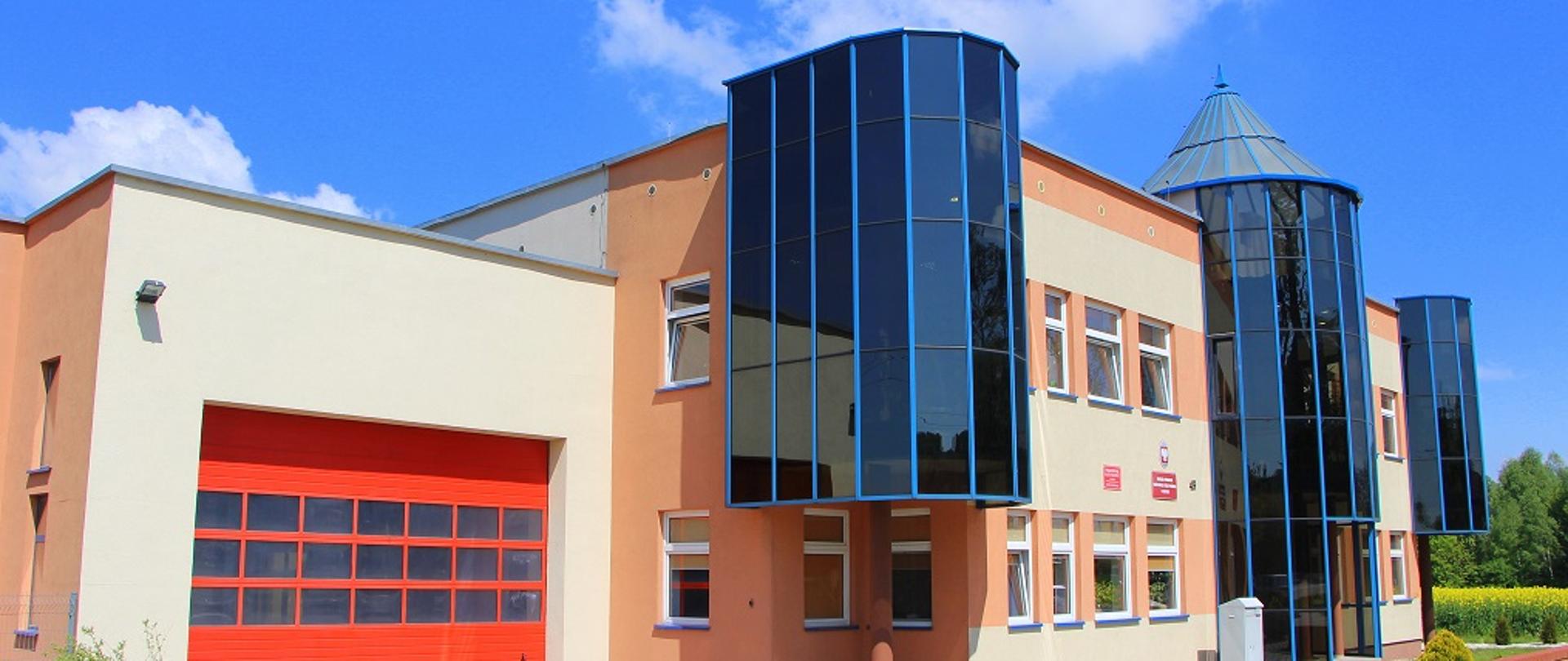 budynek komendy ze szklanymi elementami , jasna elewacja, czerwona brama garażowa