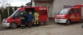 Na zdjęciu strażacy pomagają wejść seniorce do samochodu pożarniczego.