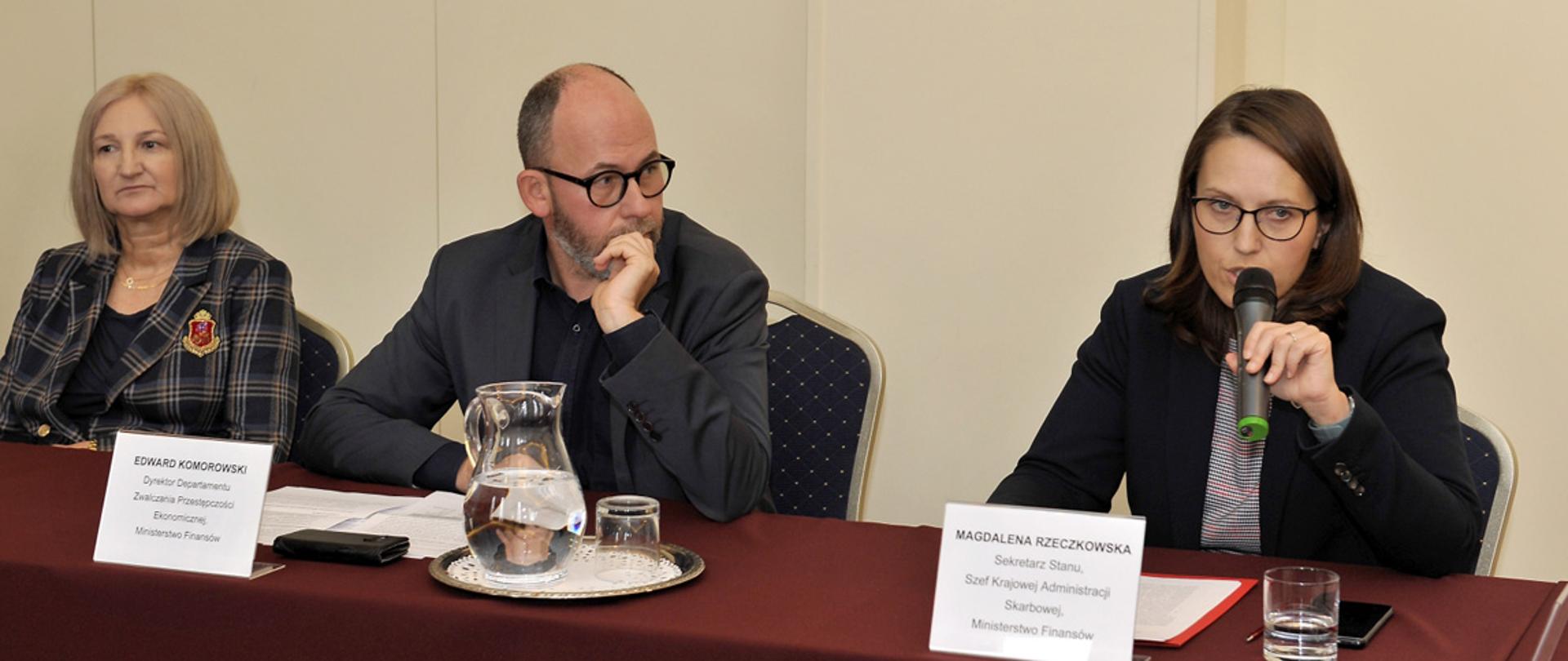 Szefowa KAS Magdalena Rzeczkowska podczas przemówienia, obok siedzą dwie osoby.