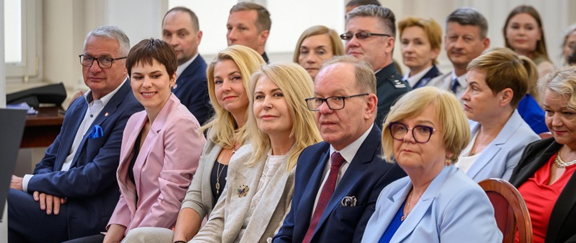 Uczestnicy debaty siedzą w sali. 