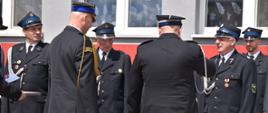 Bliskie ujęcie ceremonii wręczania odznaczeń państwowych i związkowych. Oficer Państwowej Straży Pożarnej (widoczny tyłem) gratuluje i odznacza medalami doświadczonych oraz starszych stopniem druhów ochotników, którzy z dumną postawą przyjmują wyróżnienia za wieloletnią działalność ratowniczą.