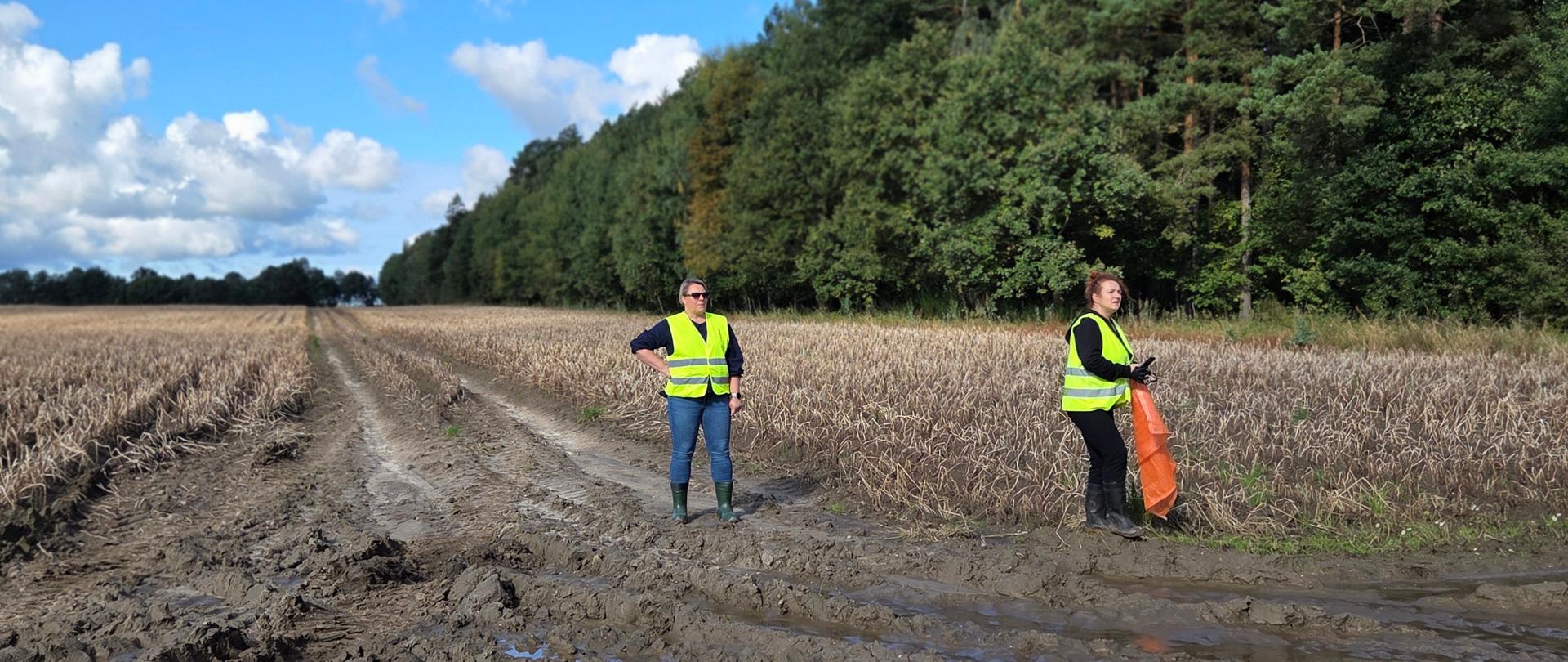 Dwie kobiety w kamizelkach odblaskowych stoją na polu 