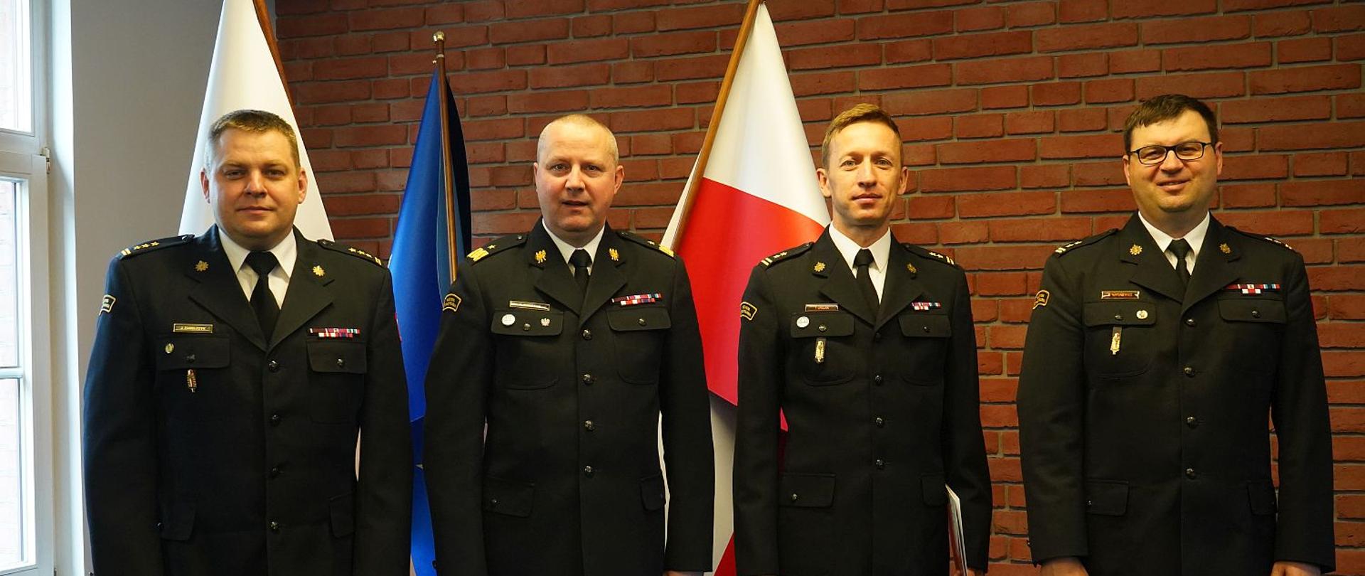 czterech strażaków stoi w szeregu, w tle flaga biało czerwona