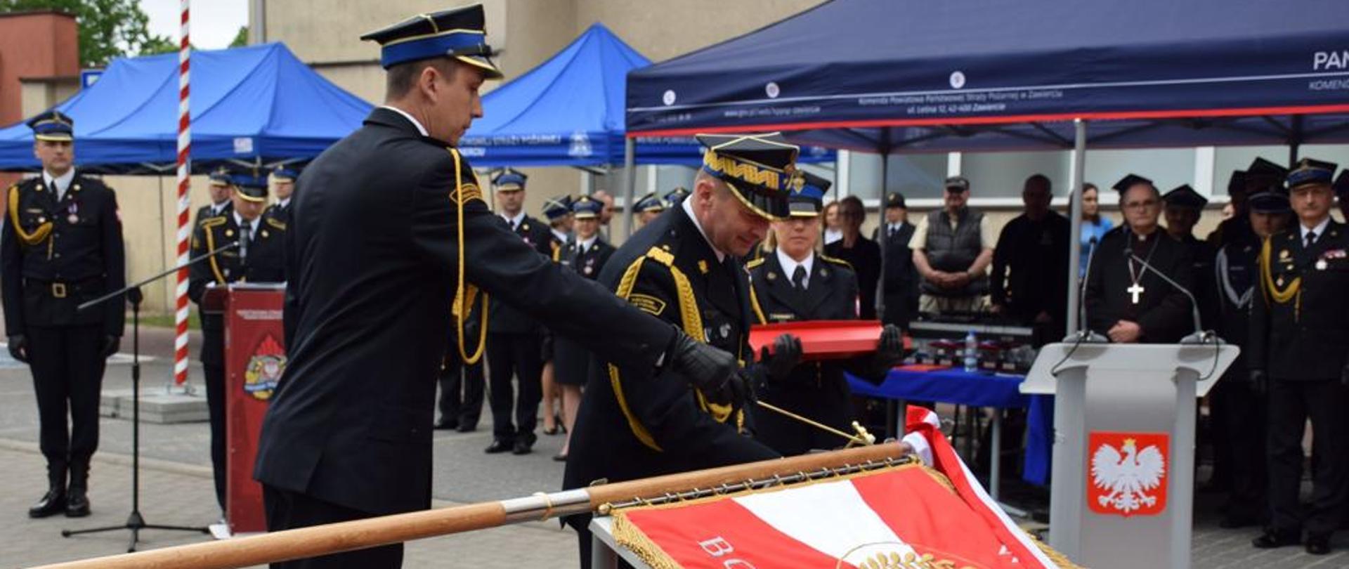 Zastępca komendanta głównego PSP nadbryg. dr inż. Adam Konieczny dokonuje wbicia gwoździka do sztandaru położonego na statywie. W tle zebrani goście