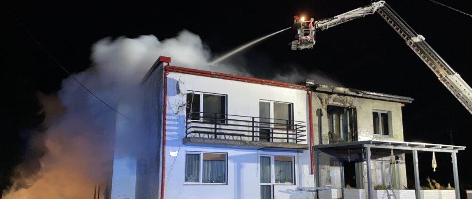 Strażacy gaszą dach budynku mieszkalnego. Podają wodę przy pomocy podnośnika hydraulicznego. 