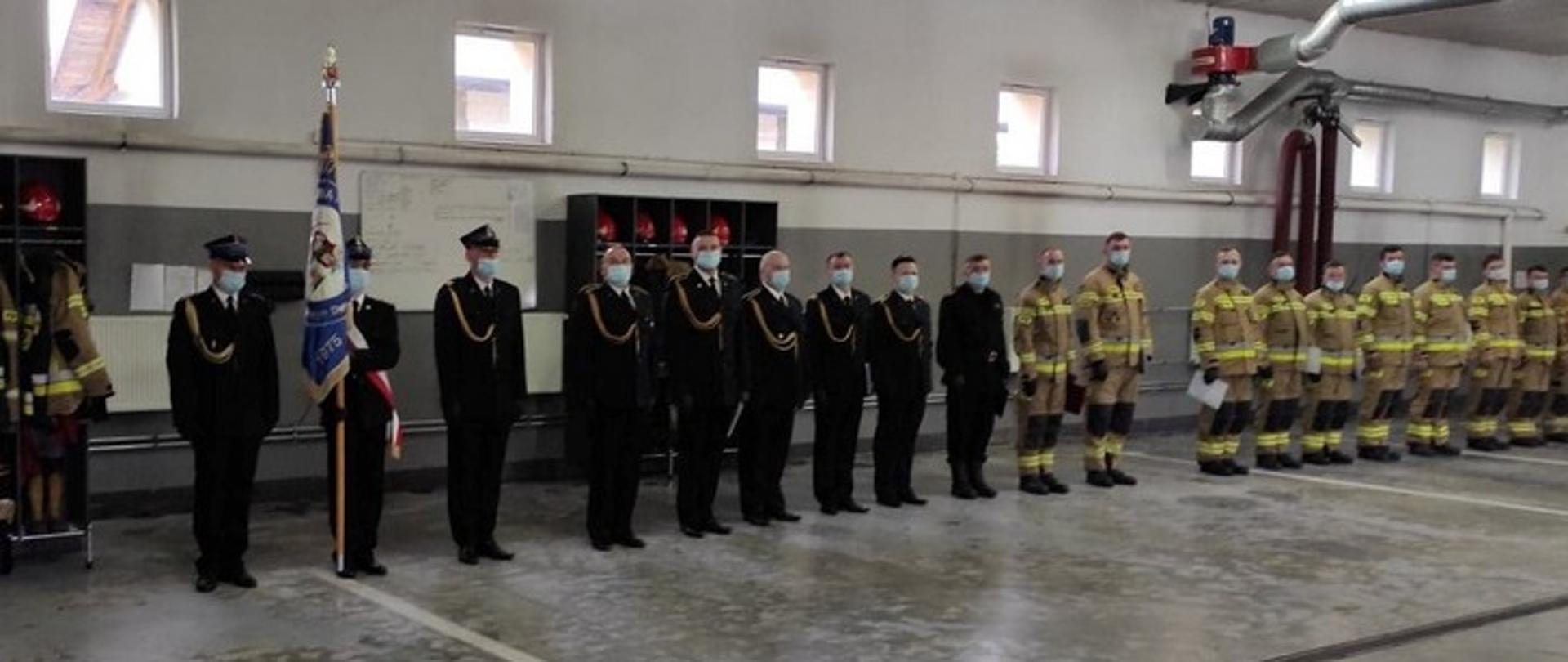 Zdjęcie przedstawia strażaków stojących w szeregu - od lewej trzech strażaków jako poczet sztandarowy w mundurach wyjściowych.