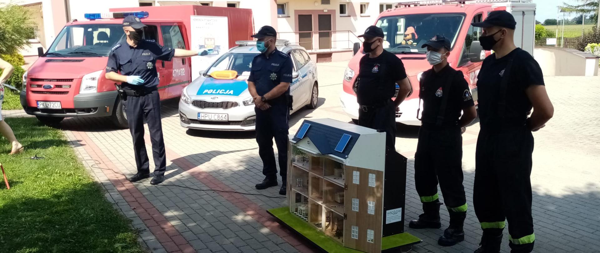 Zdjęcie przedstawia strażaków i policjantów opisujących zagrożenia na symulatorze zagrożeń