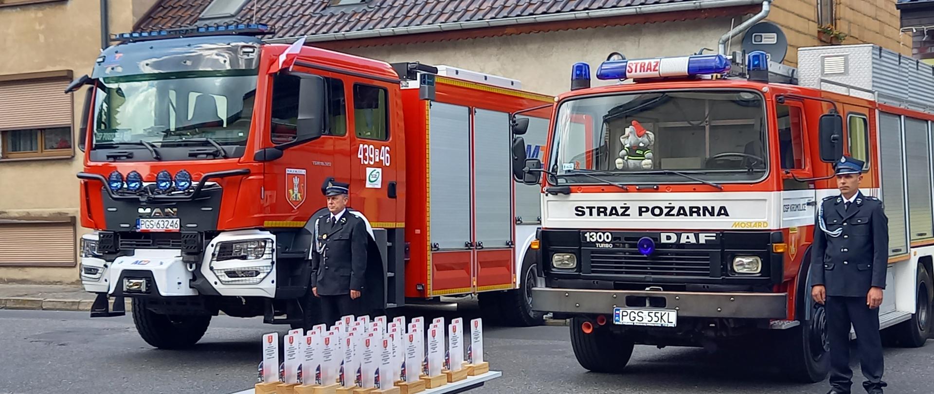 Pojazdy pożarnicze stojące na drodze. Przy nich stoją kierowcy.