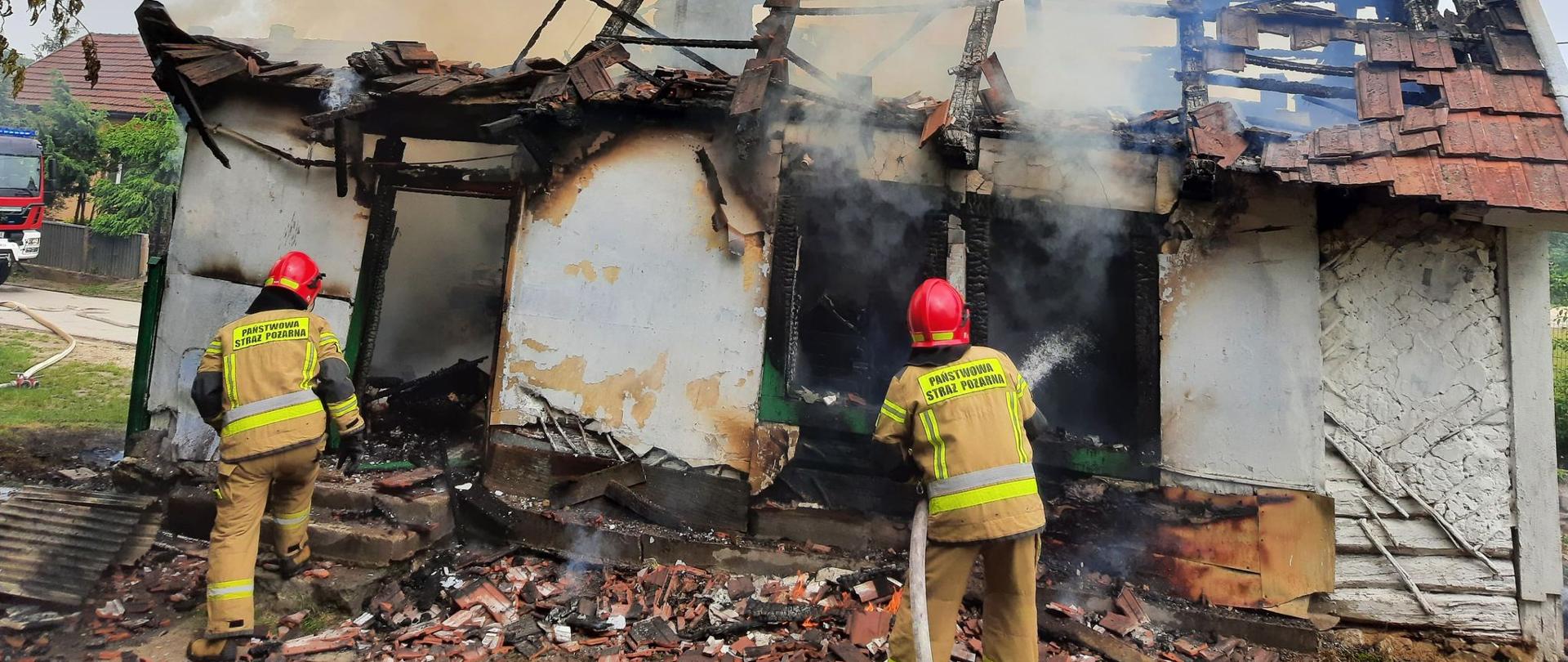 Na zdjęciu dwaj strażacy prowadzą działania gaśnicze podczas pożaru budynku mieszkalnego