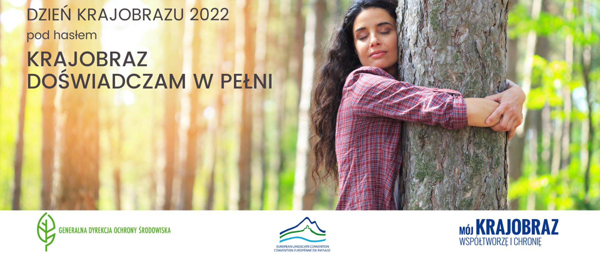 Dzień krajobrazu 2022 pod hasłem Krajobraz doświadczam w pełni. Po prawej stronie zdjęcia Kobieta w kraciastej koszuli przytula pień drzewa. W tle las.