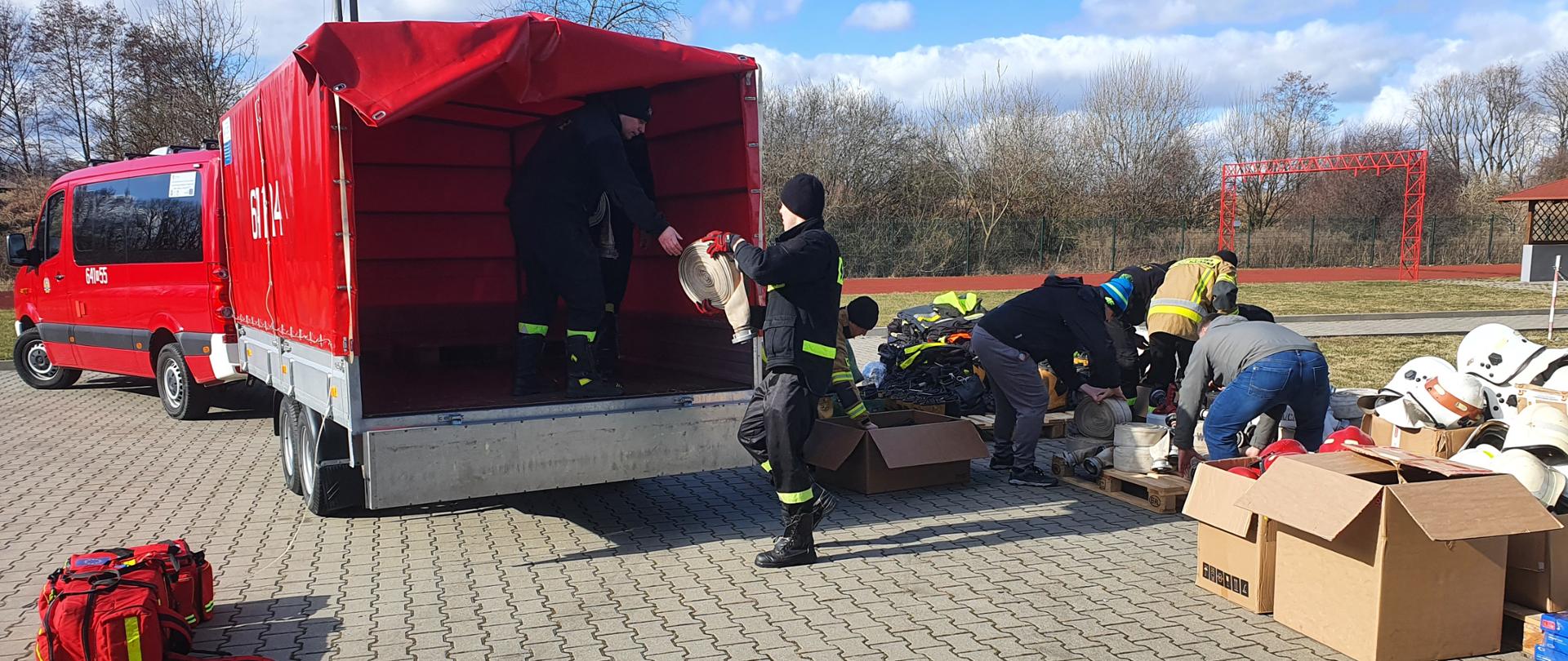 zbiórka sprzętu pożarniczego dla strażaków z Ukrainy - prace związane z przygotowaniem sprzętu pożarniczego, który przekazany zostanie dla strażaków z Ukrainy - strażacy ustawiają na paletach hełmy, węże pożarnicze i inny sprzęt na przyczepce