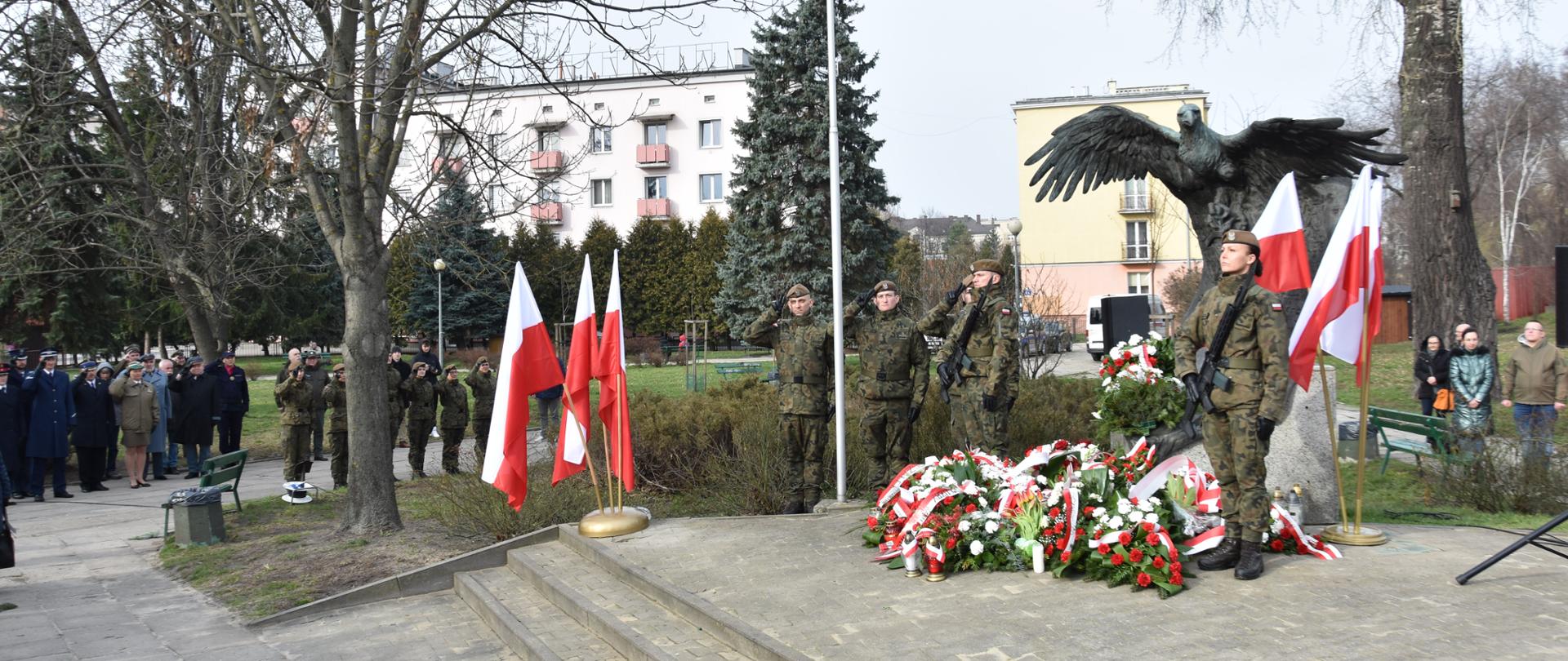 Na zdjęciu grupa żołnierze stojący pod pomnikiem. Na ziemi leżą wiązanki i znicze. 
