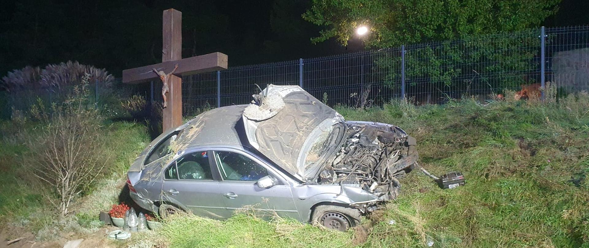 NA zdjęciu widać rozbity pojazd osobowy przy krzyżu 