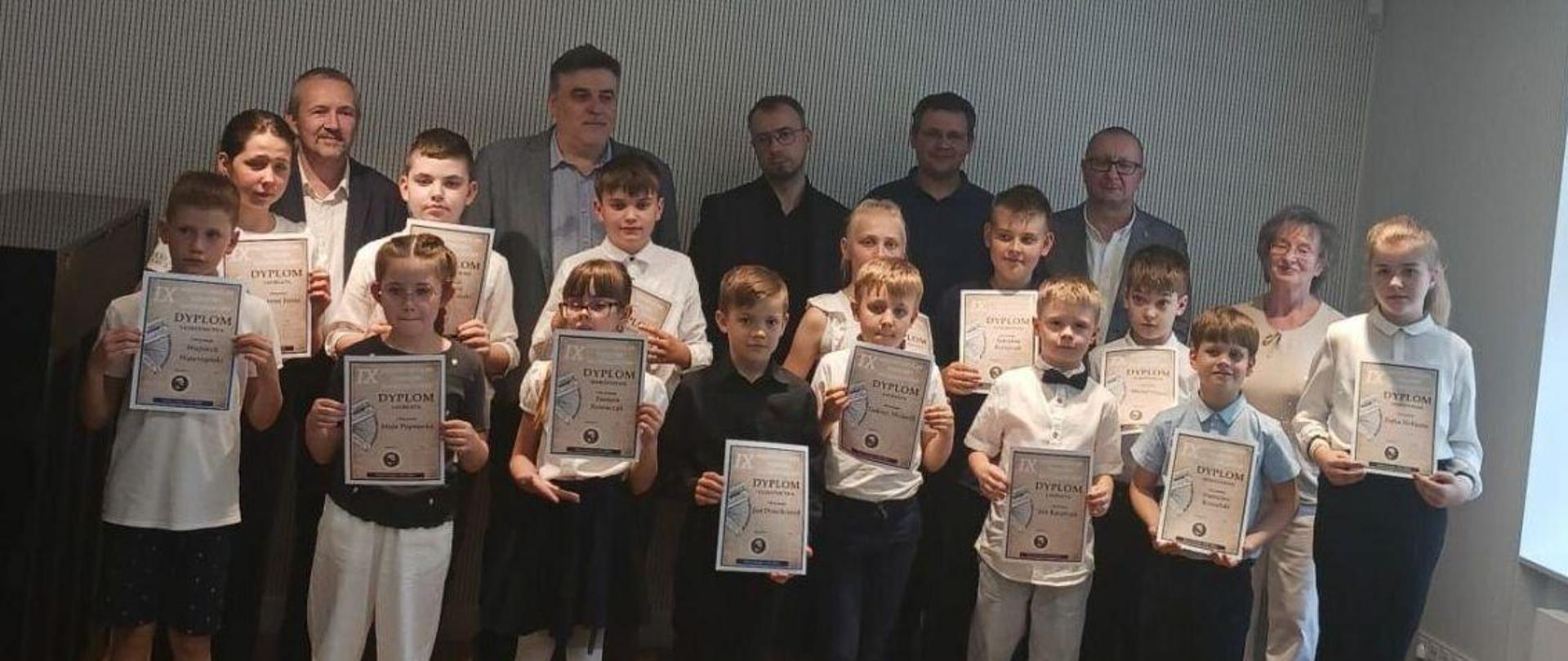 Zdjęcie grupowe uczestników konkursu akordeonowego. Uczniowie stoją w dwóch rzędach trzymając w rękach dyplomy, za nimi stoją nauczyciele.