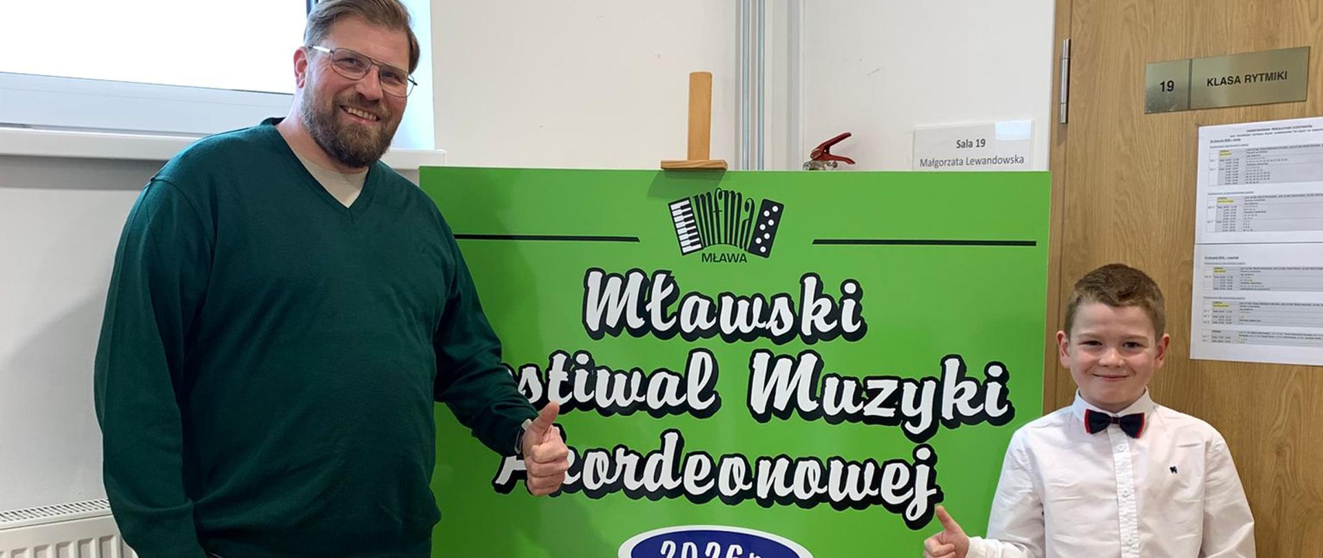 Pan Andrzej Mantyk z uczniem Hubertem Rolikiem przy banerze konkursu w Mławie