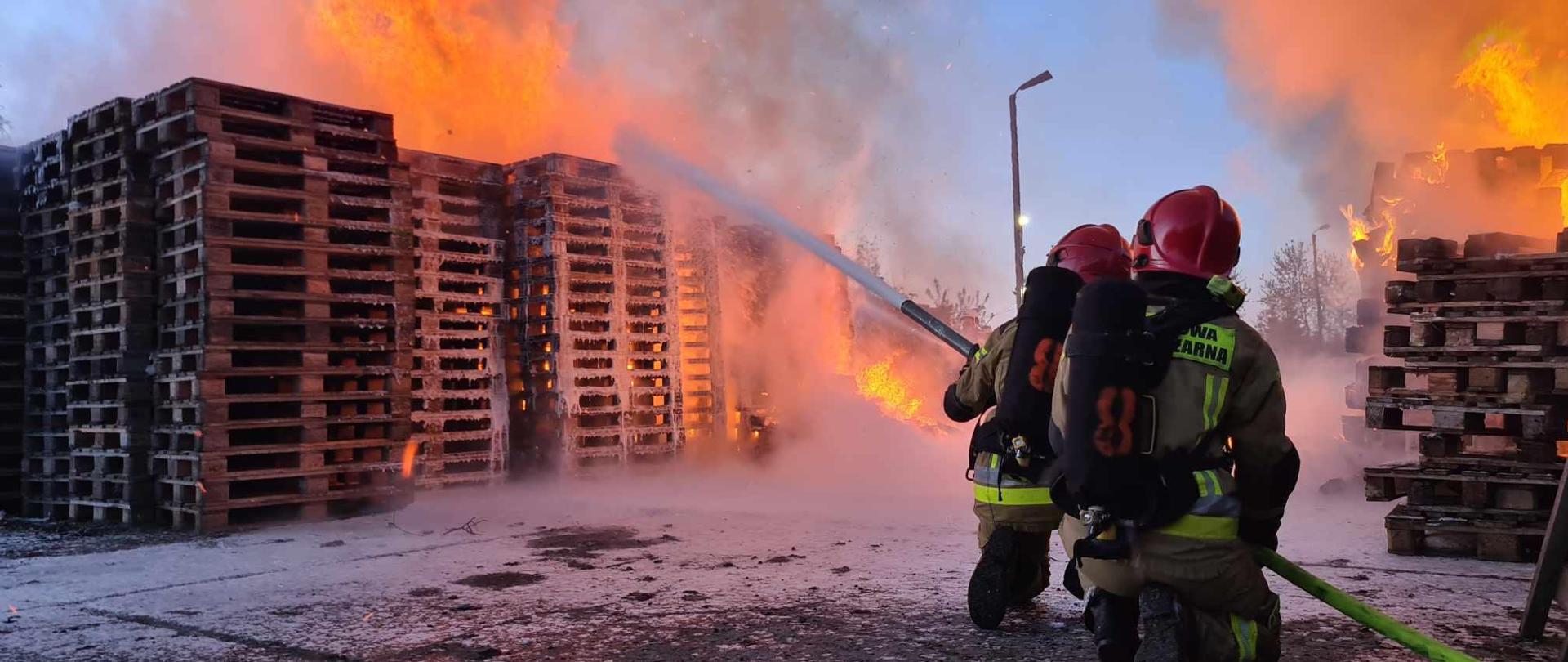 Rota strażaków podaje pianę na pożar stosu palet