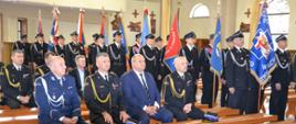 kierownictwo komendy siedzi na ławce w kościele , w tle poczty sztandarowe OSP