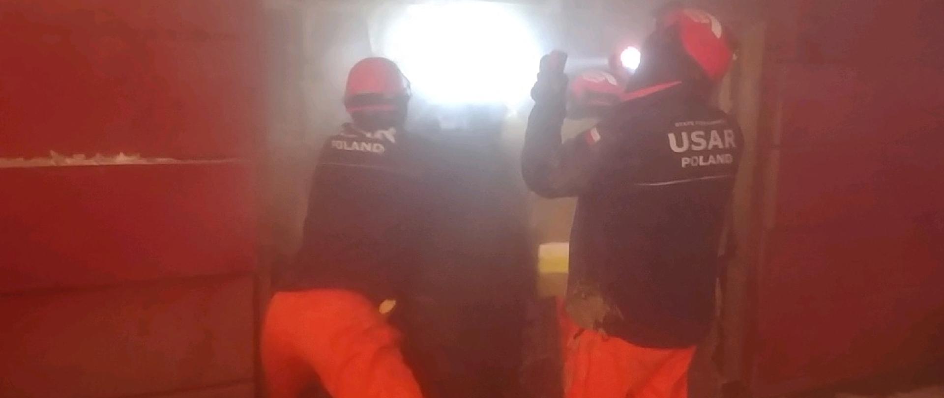 Strażacy z SGPR prowadzą działania. Jeden z nich oświetla miejsce prowadzonych działań.