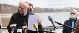 Jarosław Gowin podczas konferencji prasowej. Stoi na pomoście, pokazuje uchwałę.