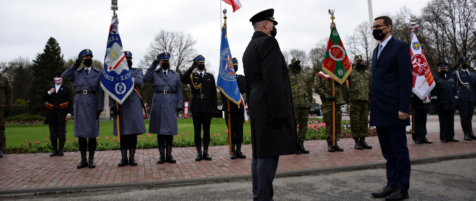 Prezes Rady Ministrów Pan Mateusz Morawiecki przyjmuje meldunek podczas uroczystości obchodów 100. rocznicy wybuchu III Powstania Śląskiego w Parku Śląskim. W tle poczty sztandarowe policji, straży pożarnej, wojska.