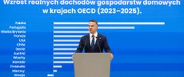 Konferencja prasowa Rzecznika Rządu Adama Szłapki 02.09.2025 r. W tle ekran z tabelą z wykresem "Wzrost realnych dochodów gospodarstw domowych w krajach OECD (2023-2025).