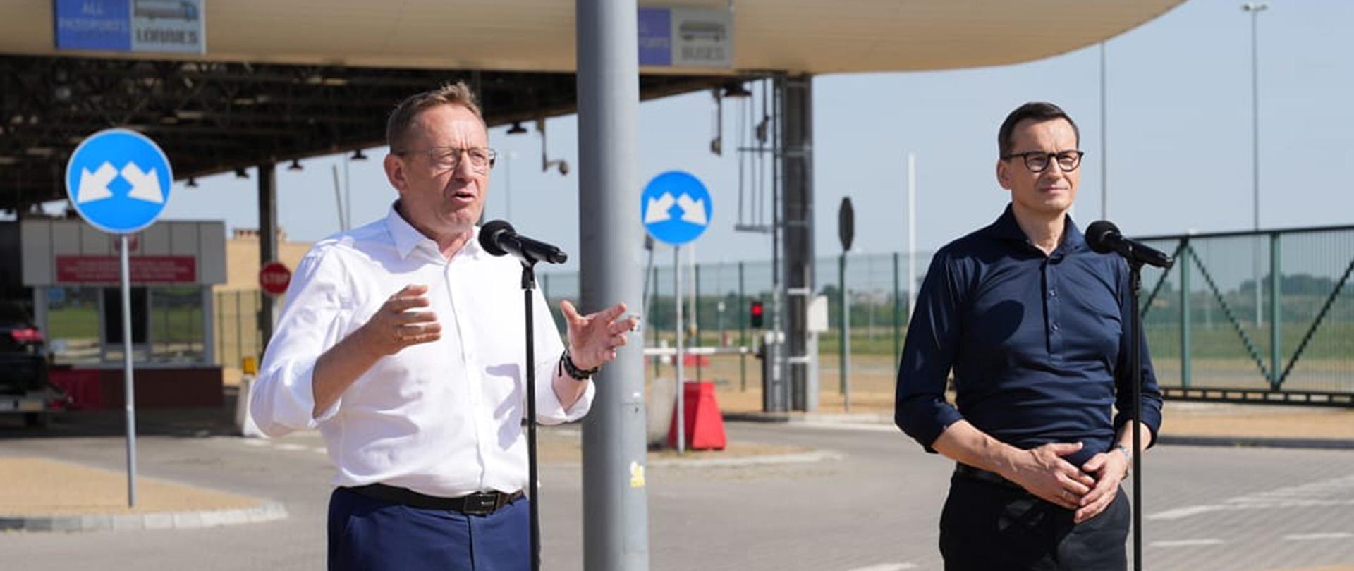 Minister Robert Telus oraz premier Mateusz Morawiecki stojący przy mikrofonach, w tle przejście graniczne